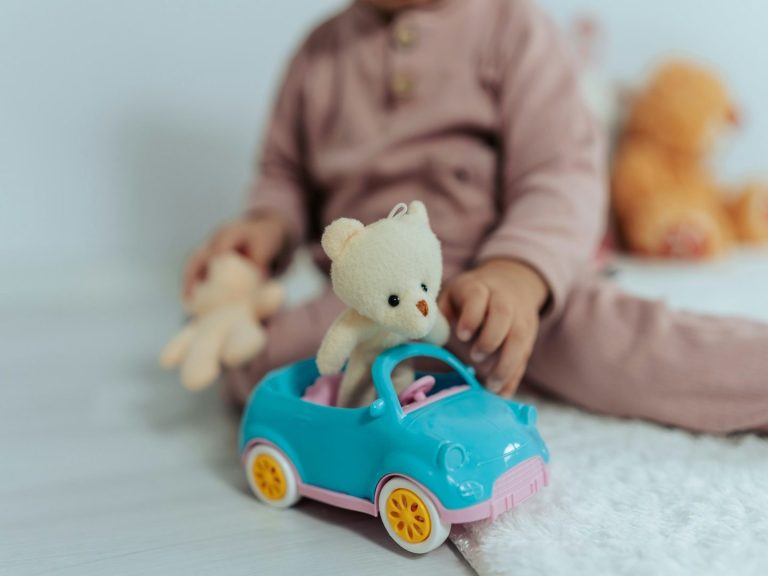Un enfant joue avec une voiture en plastique, portant un ours en peluche à l'intérieur.